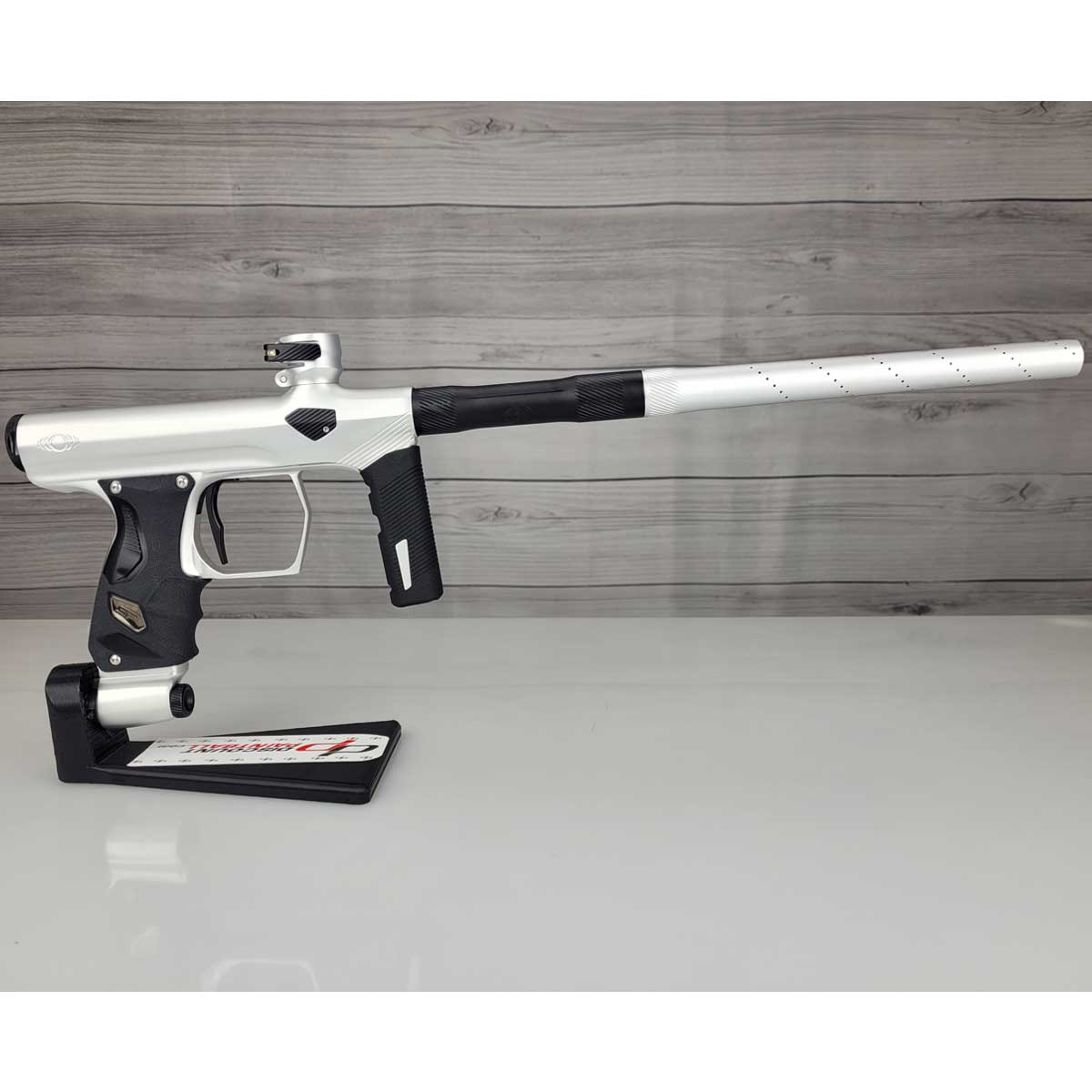 Right side USED Shocker Era Silver black paintball marker in a stand on a woodgrain background.