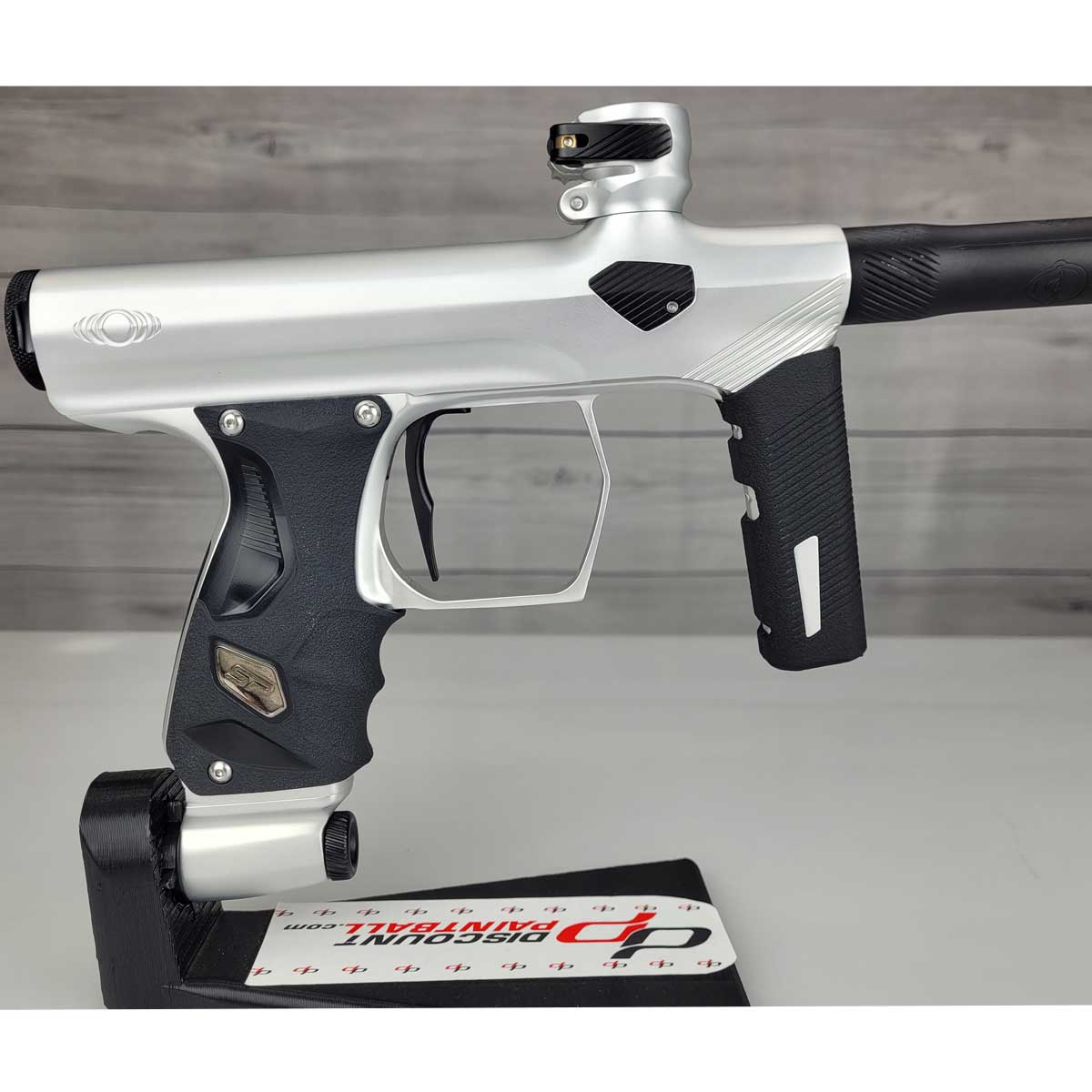 Right side body USED Shocker Era Silver black paintball marker in a stand on a woodgrain background.