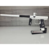 Left side USED Shocker Era Silver black paintball marker in a stand on a woodgrain background.
