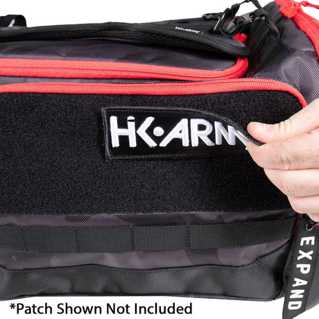 Black and red Paintball Expand 75L Roller Gear bag Shroud Black Red on a white background with a hand removing a patch