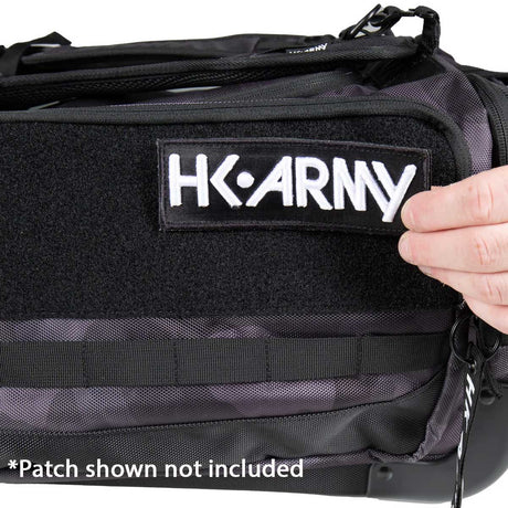 Close-up of a black tactical-style bag with a Velcro patch area and the embroidered text 'HK ARMY' on the front. A hand is touching the patch, and a note at the bottom says '*Patch shown not included'.