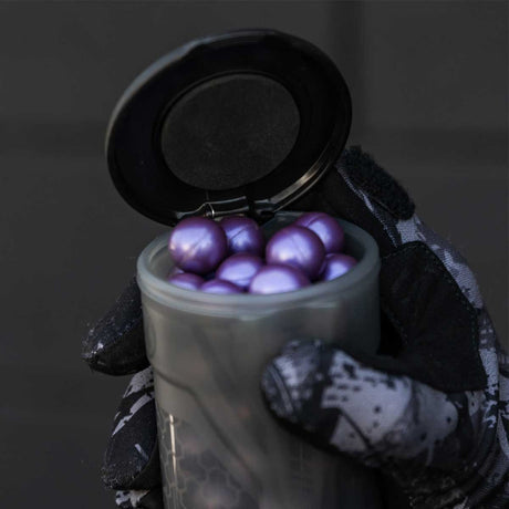 Open tube containing purple paintballs being held by a gloved hand HK Army Apex 150 Round Paintball Pods Light Smoke on a dark background
