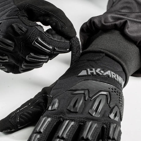 Person putting on a Pair of black HK Army Hardline Armored Full Finger Gloves Tactical for paintball, airsoft and other sports on a white background
