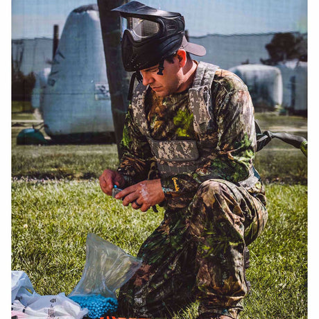 Person dressed in camo with a paintball mask loading a Left  Black and silver T4E Walther PPQ .43 Cal 8rd CO2 Paintball Magazine on a grassy background